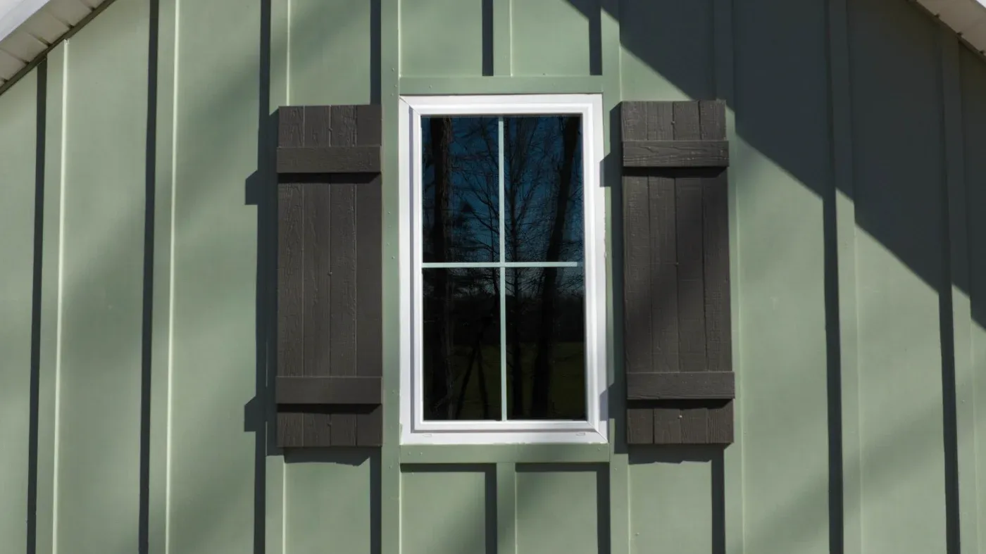 A new window installed on a green house with black shutters.