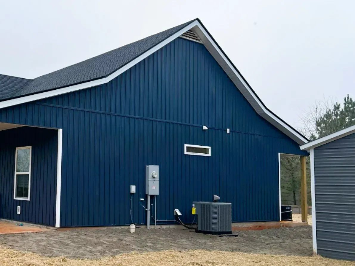 A large residential exterior wall features deep blue vertical board-and-batten panels contrasted by crisp white trim, highlighting a modern and dramatic siding replacement project.