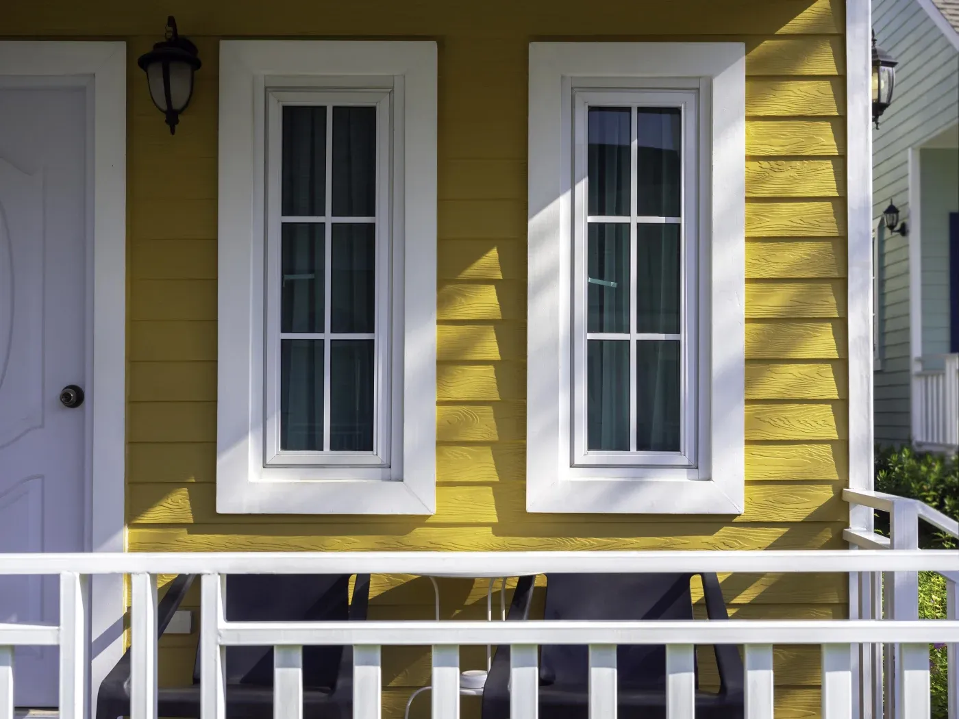 Two white windows in white frames on a yellow house with a white porch.