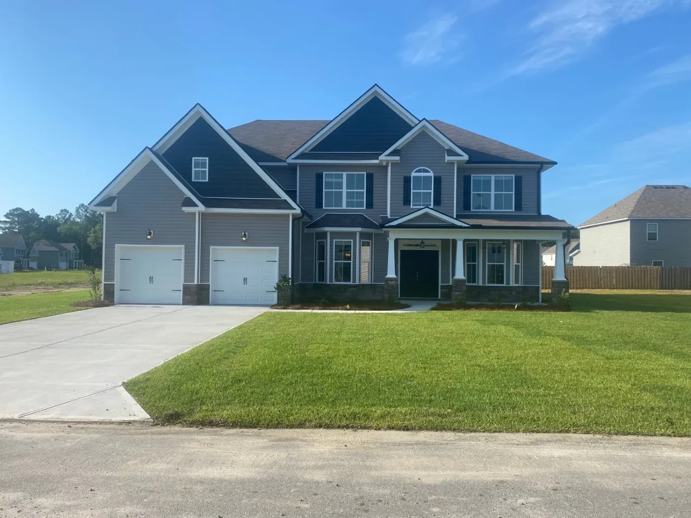 A two-story gray house with white garage doors, white windows, black shutters, white trim, and a shingle roof.