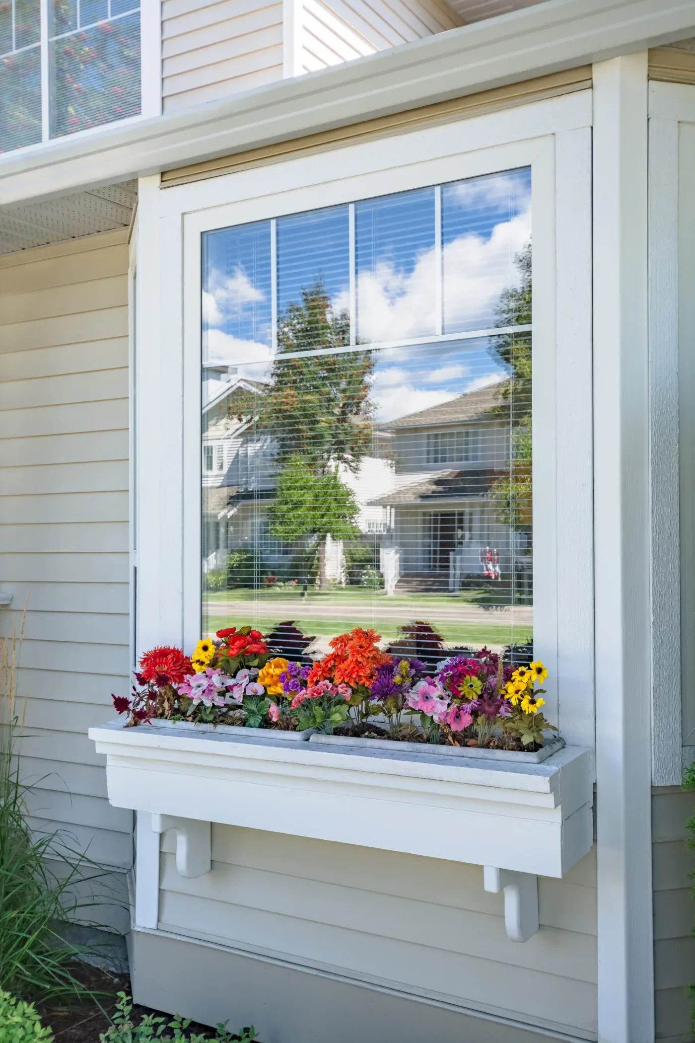 A white window with a white frame on a white house with flowers underneath.