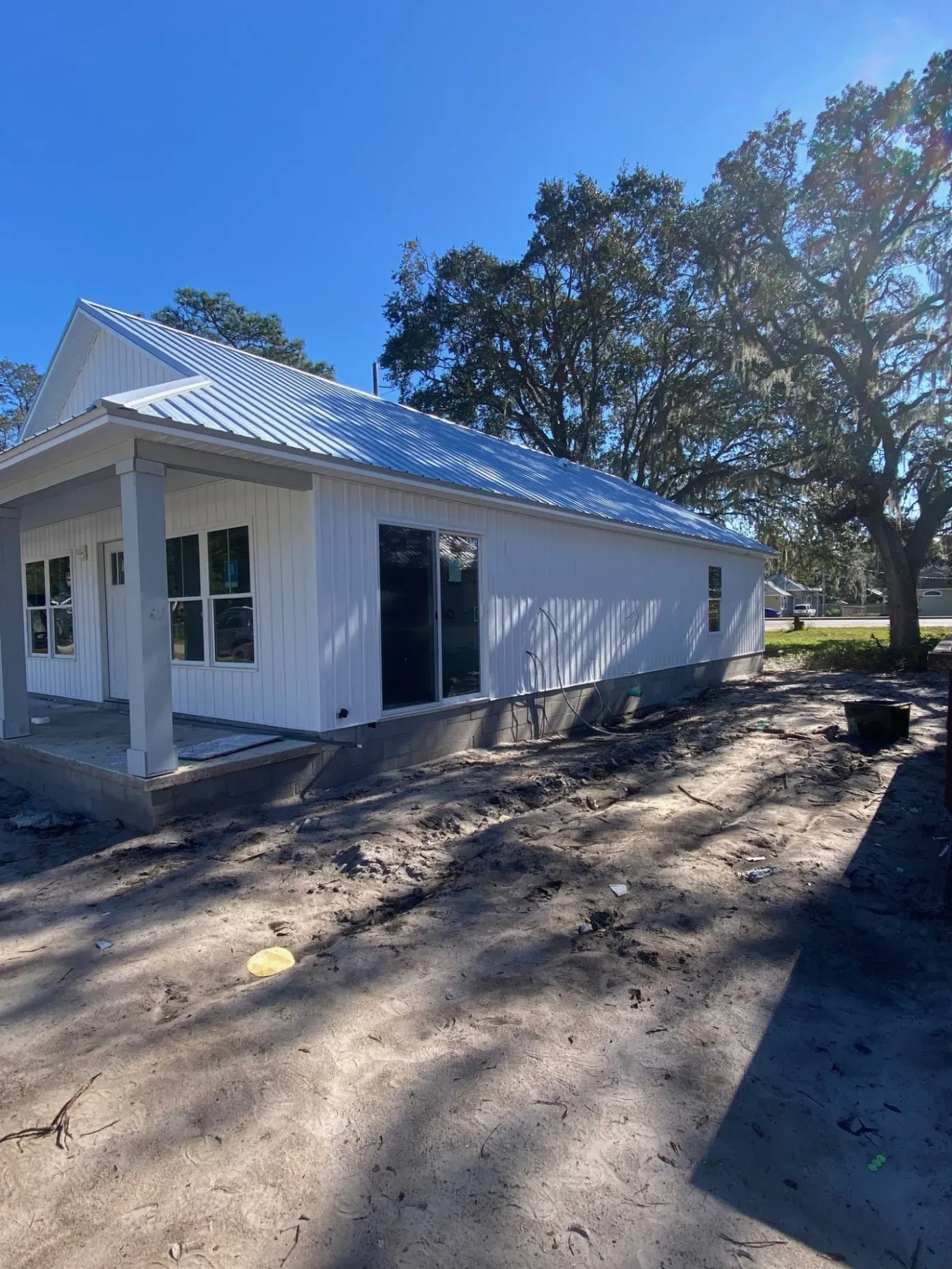 A corner view of a new white house with a metal roof, a front porch, and white windows.