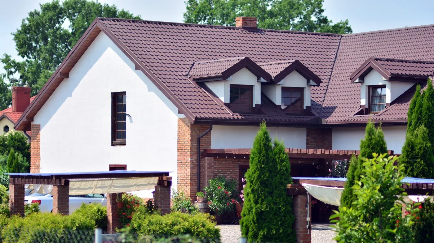 A brown roof with dormers on a white stucco and brick house.