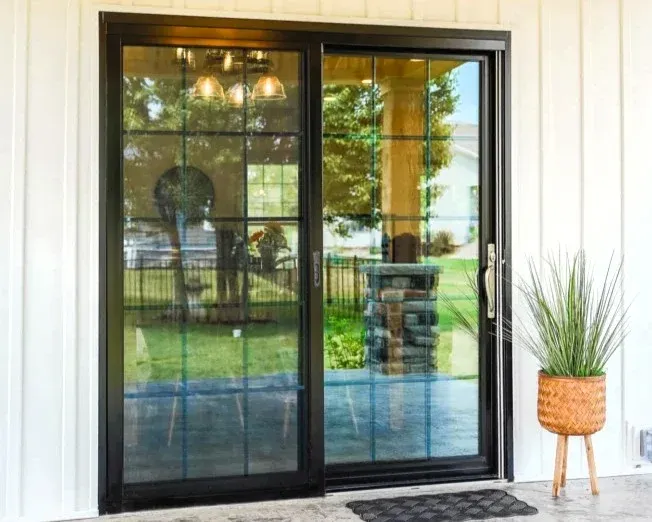 A black sliding glass door with a gold handle on a white house.