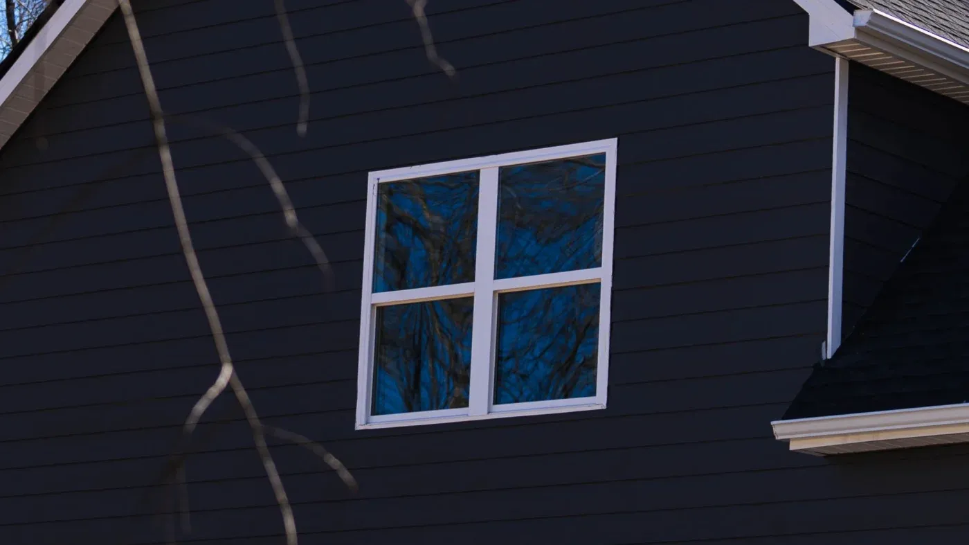 A white-framed window in a house with dark blue siding.