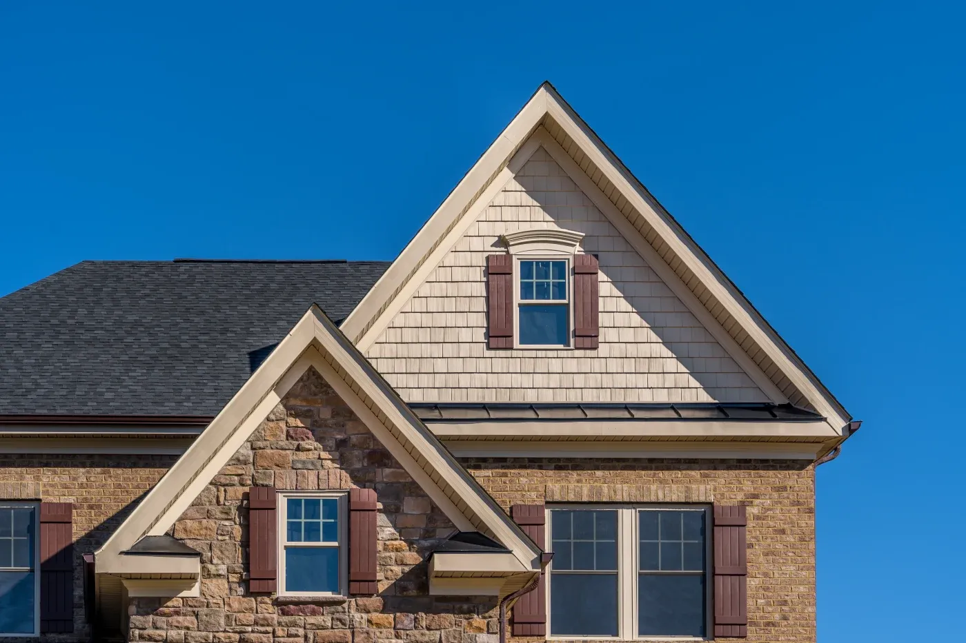 Double Triangle Gable With Double Hung Sash Window With Complementing Shutters, Decorative Arched Trim, Shake And Shingle And Architectural Stone Siding, Brown Eaves Through System, Fascia, Soffit