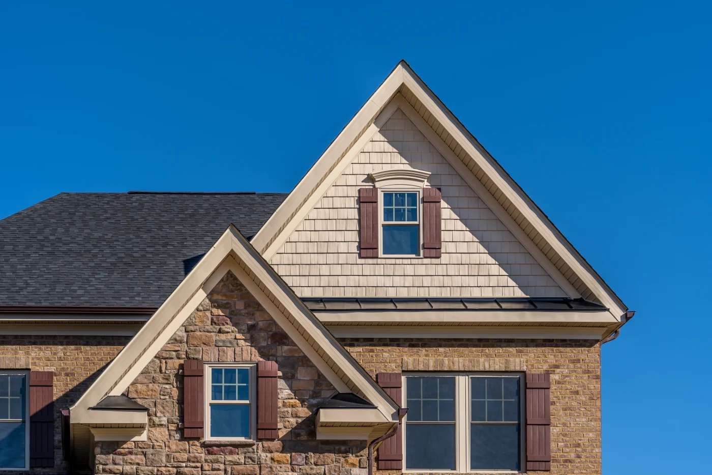 Double Triangle Gable With Double Hung Sash Window With Complementing Shutters, Decorative Arched Trim, Shake And Shingle And Architectural Stone Siding, Brown Eaves Through System, Fascia, Soffit