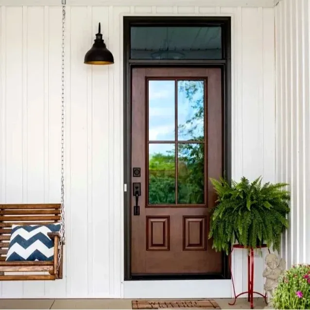 A brown entry door with glass inserts and a black handle on a white house.
