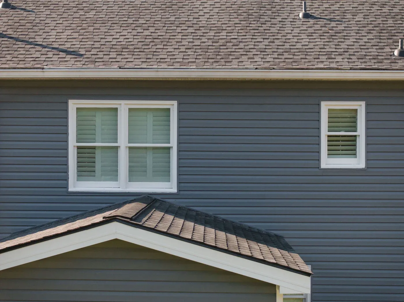The top of a gray house with an asphalt shingle roof and white windows.