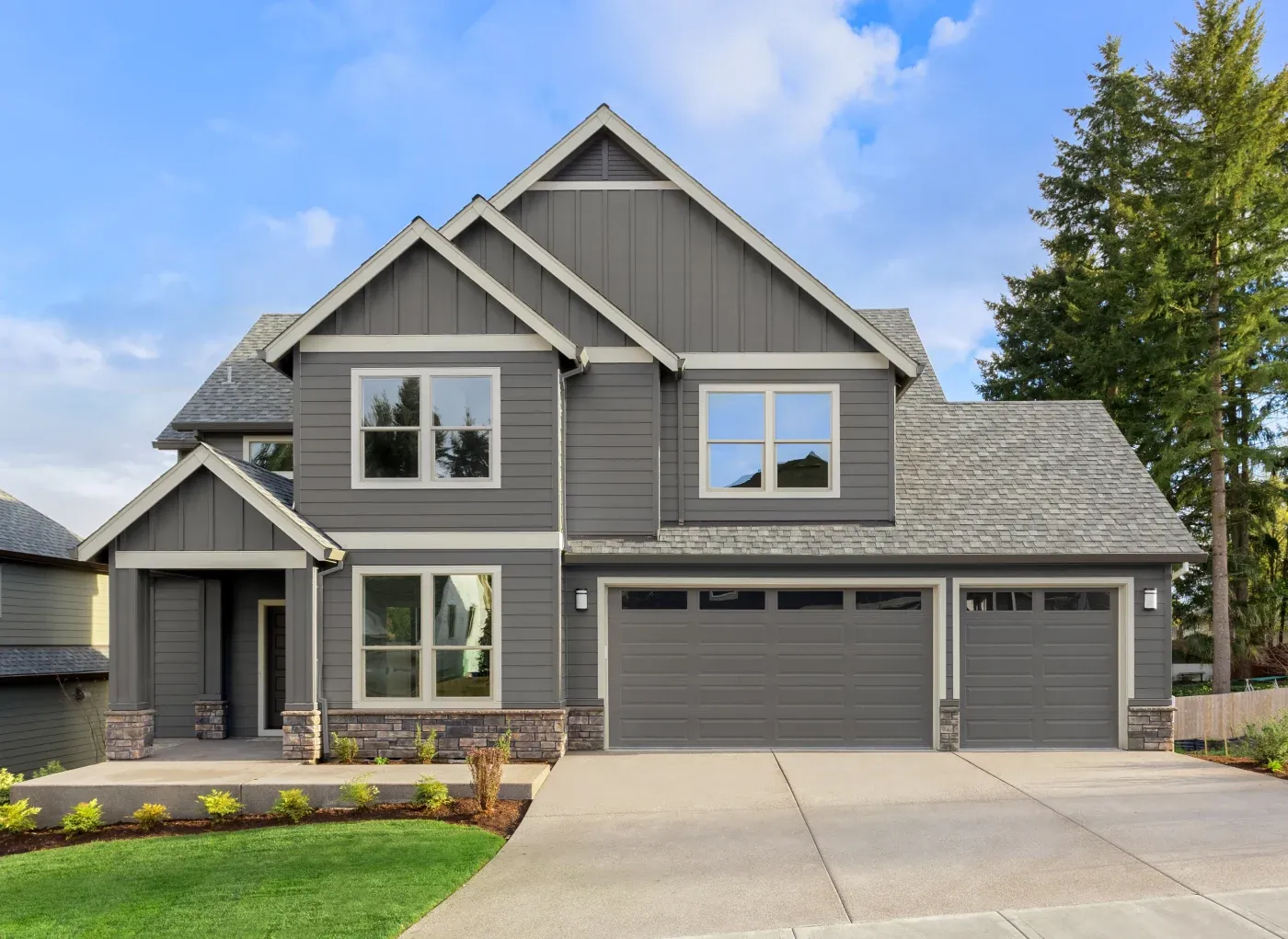 Front Exterior Of New Home On Sunny Day. Features Covered Porch, Three Car Garage, And Gables
