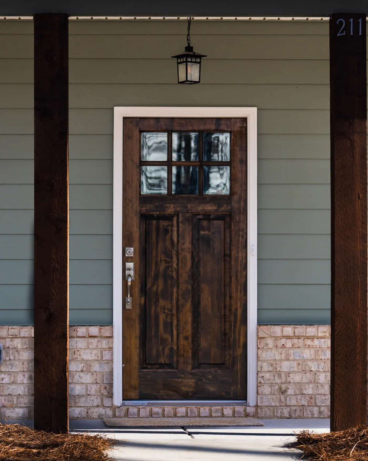 A close-up of a wood front entry door against a home with sage green James Hardie siding