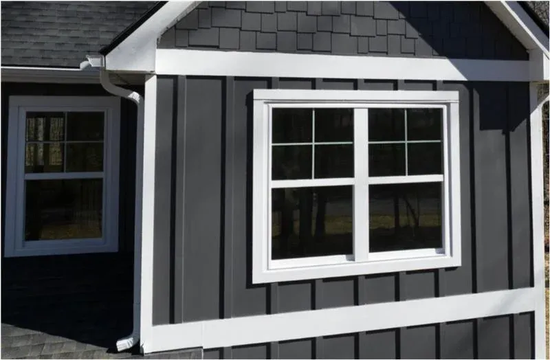 A close-up view of the upper floor of a dark gray house with white windows and white trim.