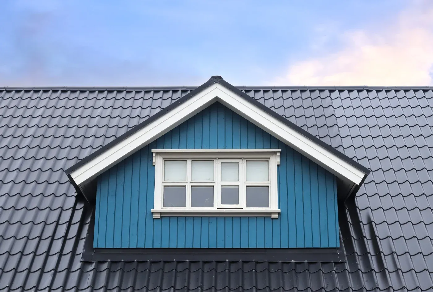 A close-up view of a metal roof on a blue house with windows.