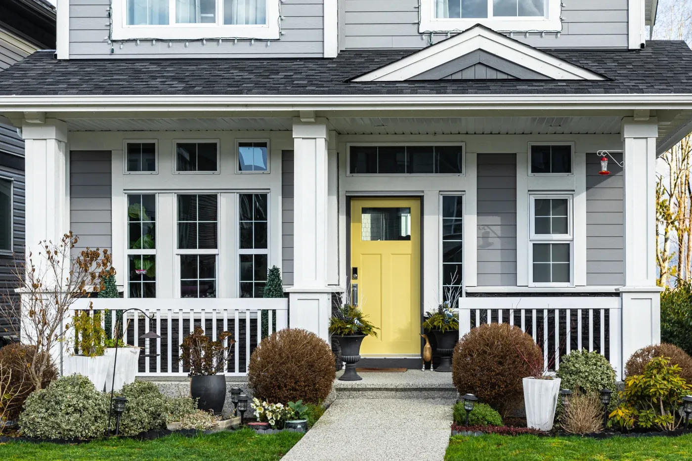 The front of a house with gray and white James Hardie siding and a yellow entry door.
