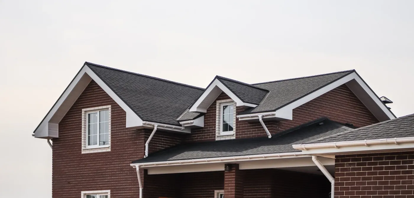 A close-up view of an asphalt shingle roof on a two-story brick house.