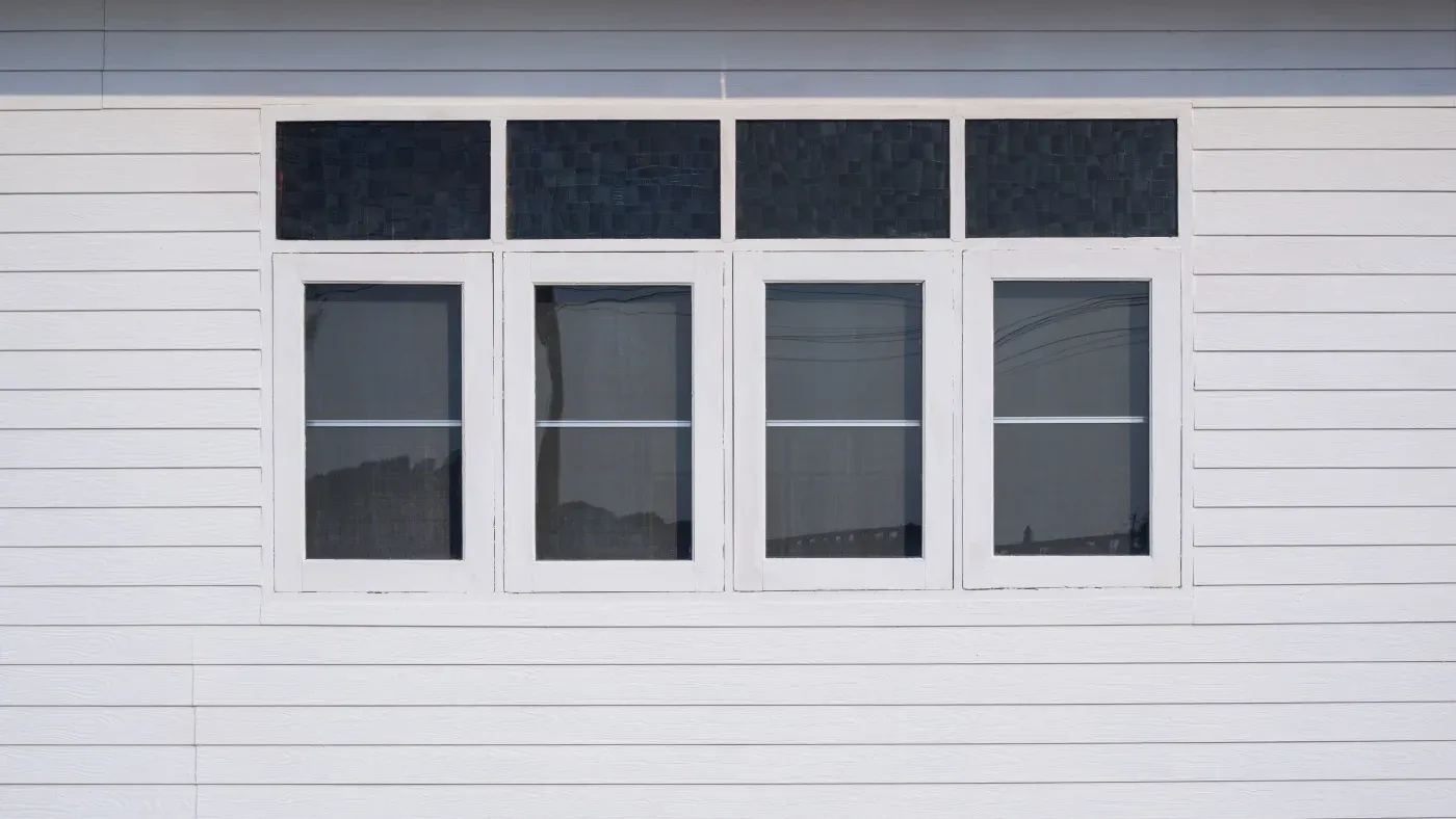 Four white windows on the side of a white house.