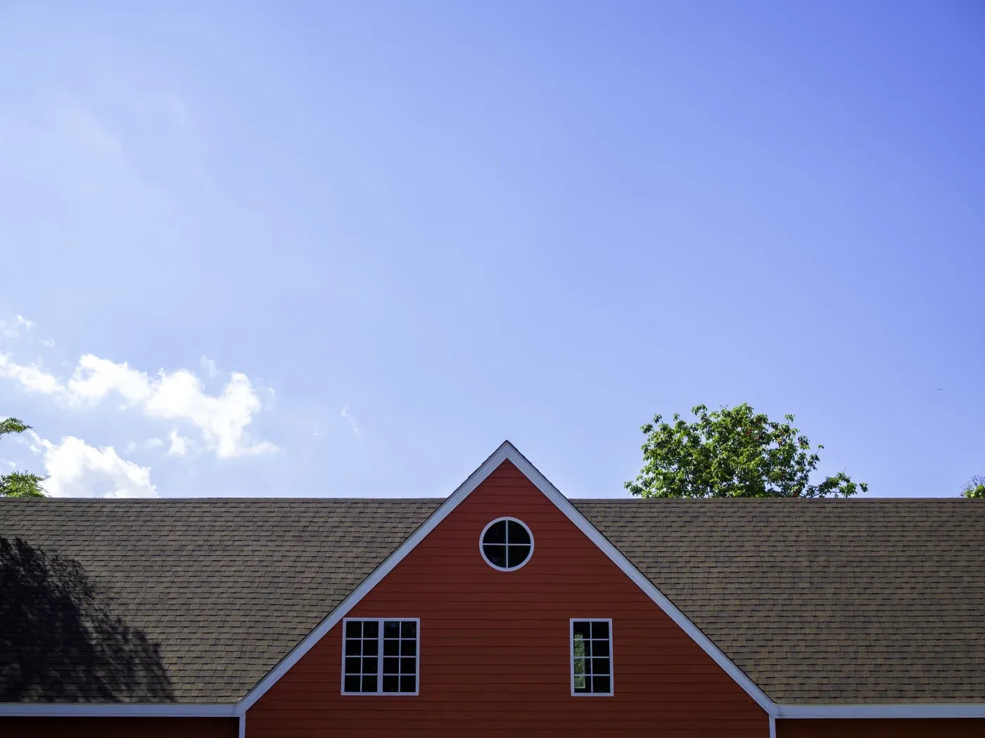 A close-up view of an asphalt shingle roof on an orange house under a blue sky.