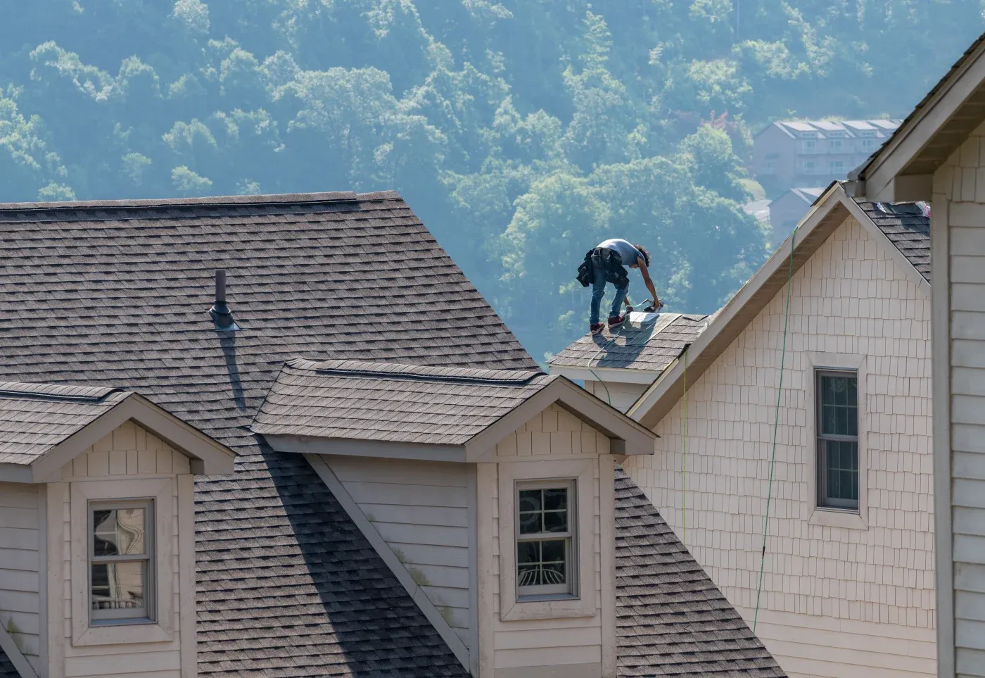 A professional contractor uses a nail gun to install shingles on the peak of a two-story home's roof.