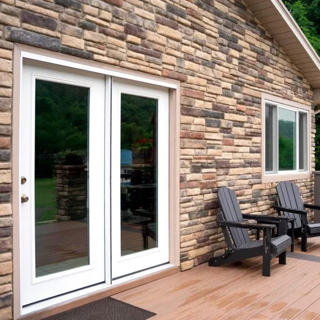 The back porch of a stone house with white doors and a white window.