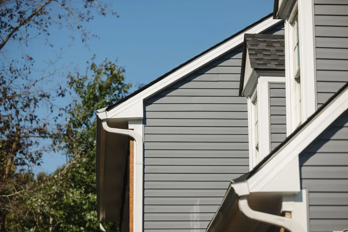 A side view of a gray house with two white dormer windows.