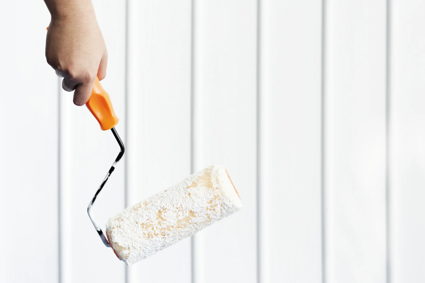 A paint roller in front of freshly finished siding