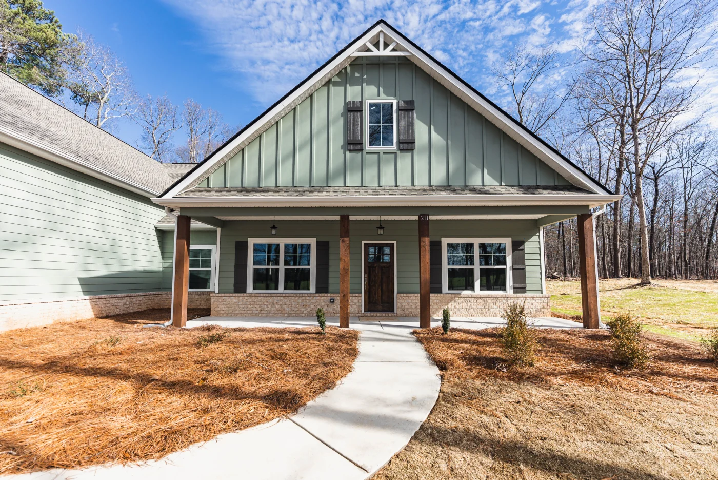 A concrete walkway curves toward a charming front porch framed by wooden pillars and Sage green board and batten siding, exemplifying the quality upgrades delivered by a professional remodeling contractor.