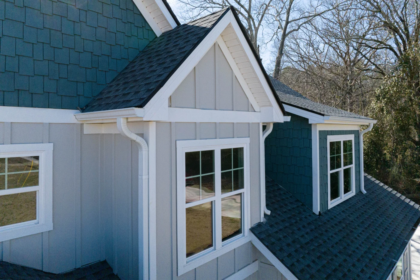 This high-angle view showcases clean gables, crisp white gutters, and freshly installed architectural shingles on a multi-level home, reflecting the precision of a professional roofing service.