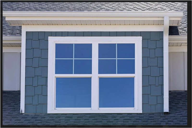 A double-hung window with a crisp white frame sits perfectly balanced within a section of light gray vertical board and batten siding, exemplifying a seamless and high-quality window replacement.