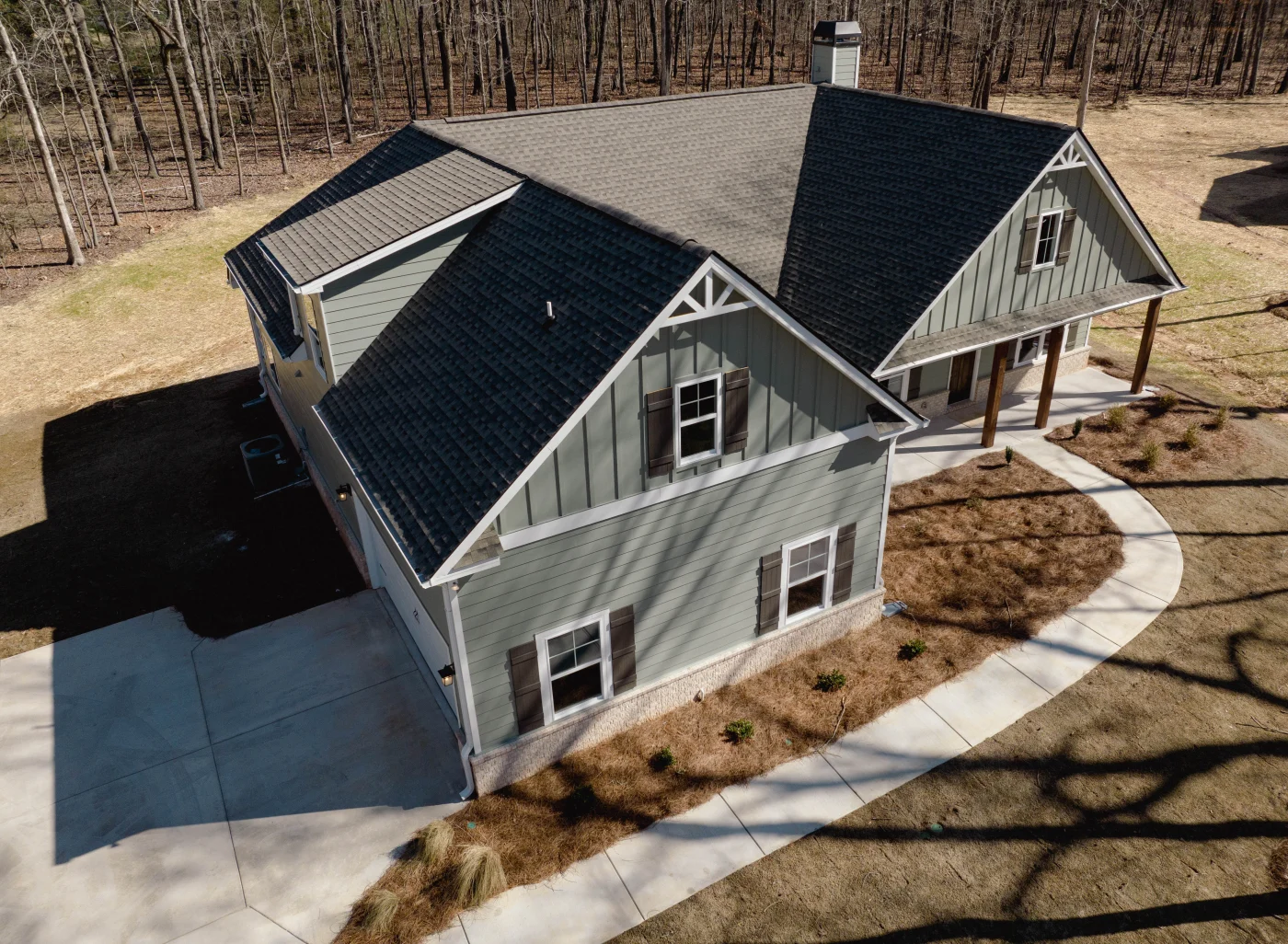 An aerial angle captures a beautiful home with Sage green siding, window shutters, and a newly paved driveway and concrete walkway, highlighting the expertise of professional new construction services.