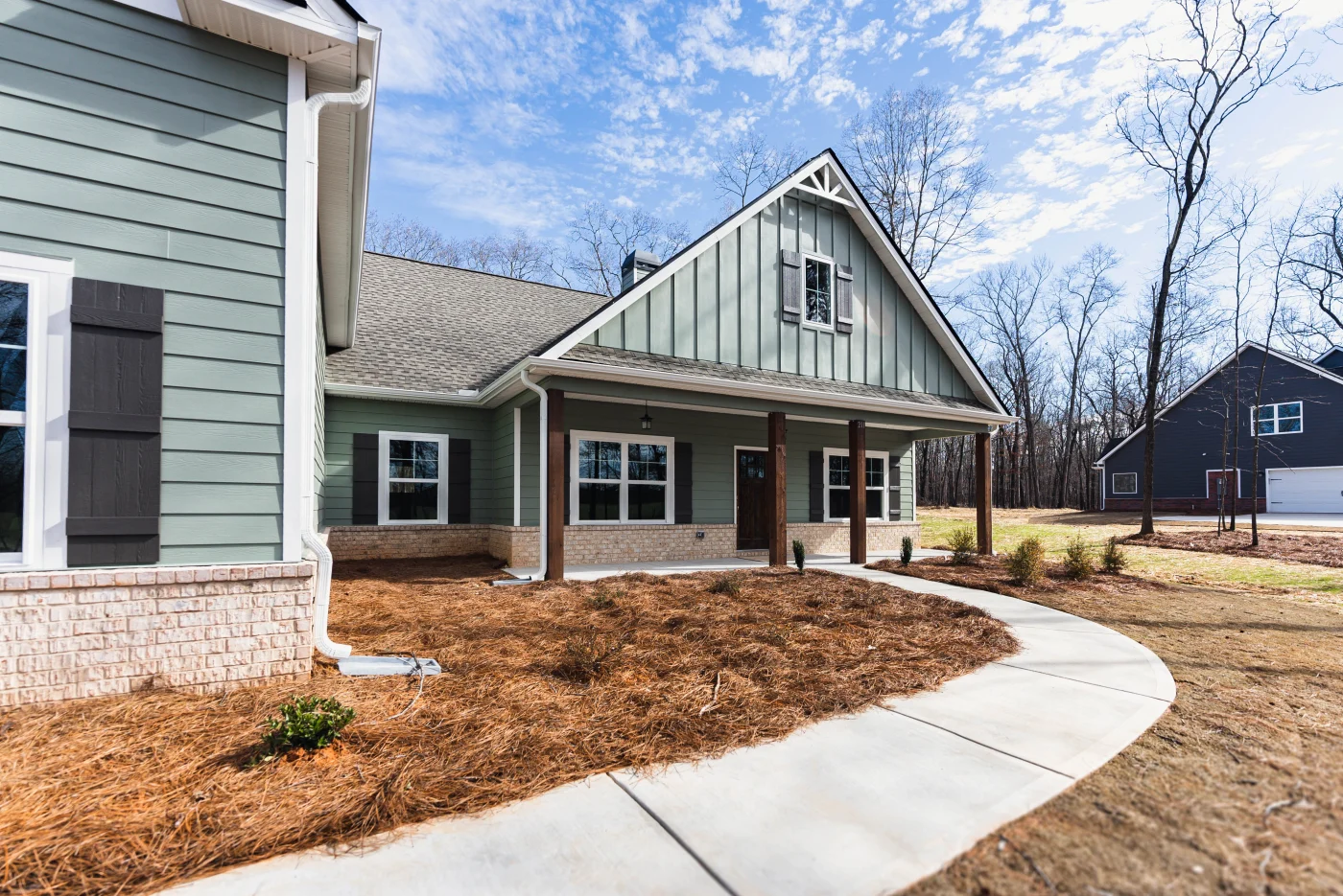 A curving concrete walkway leads toward a beautiful ranch-style home featuring sage green horizontal lap siding perfectly balanced by vertical board and batten panels on the gabled peak.