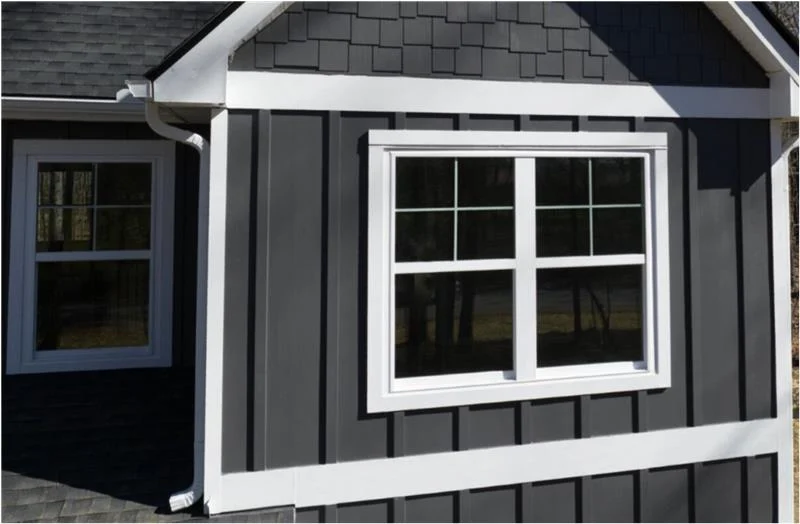 White-trimmed double-hung windows stand out sharply against dark gray board and batten cladding and matching shake accents, showcasing the clean lines of a professional siding service.