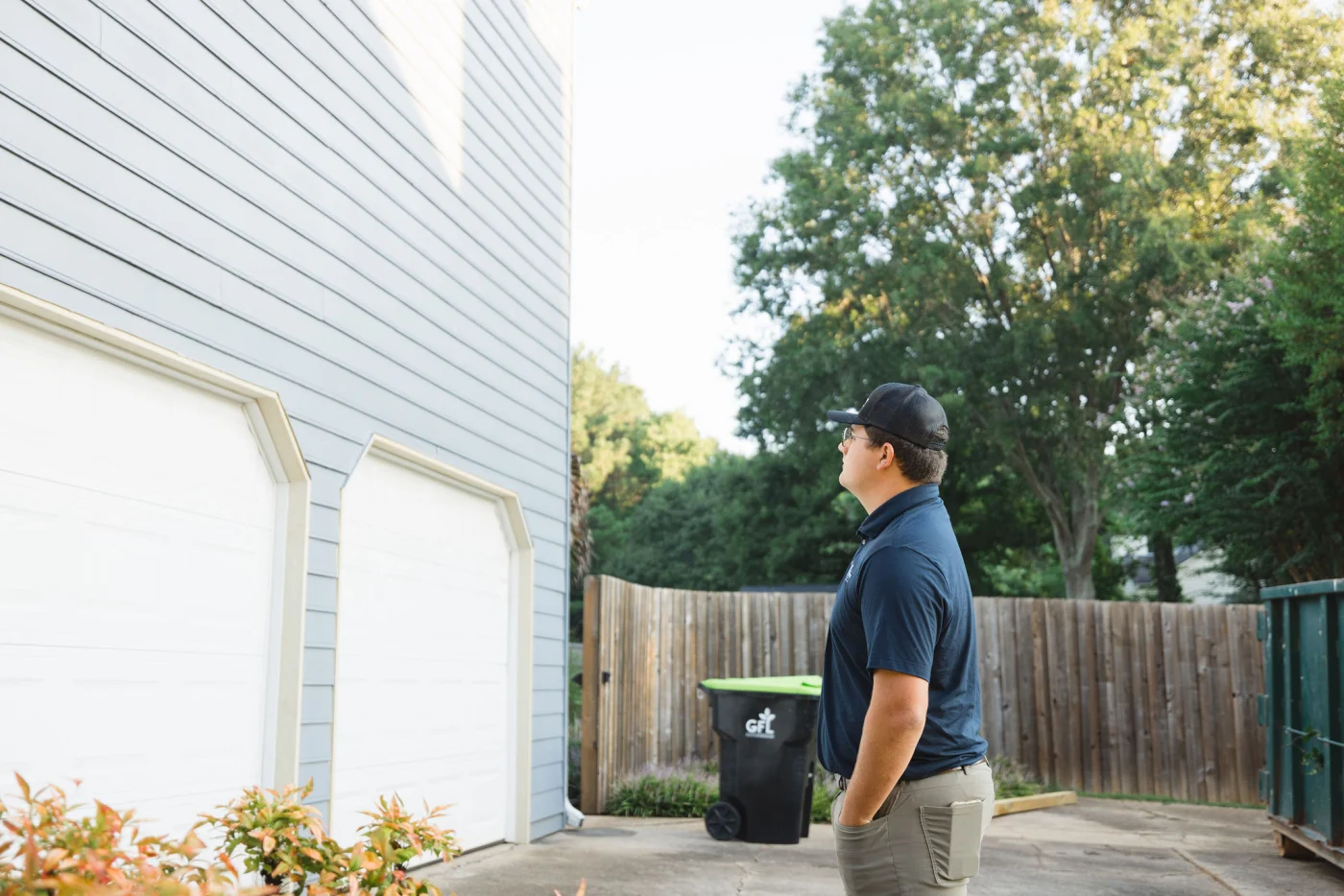 A remodeling contractor assessing light gray siding above two white garage doors