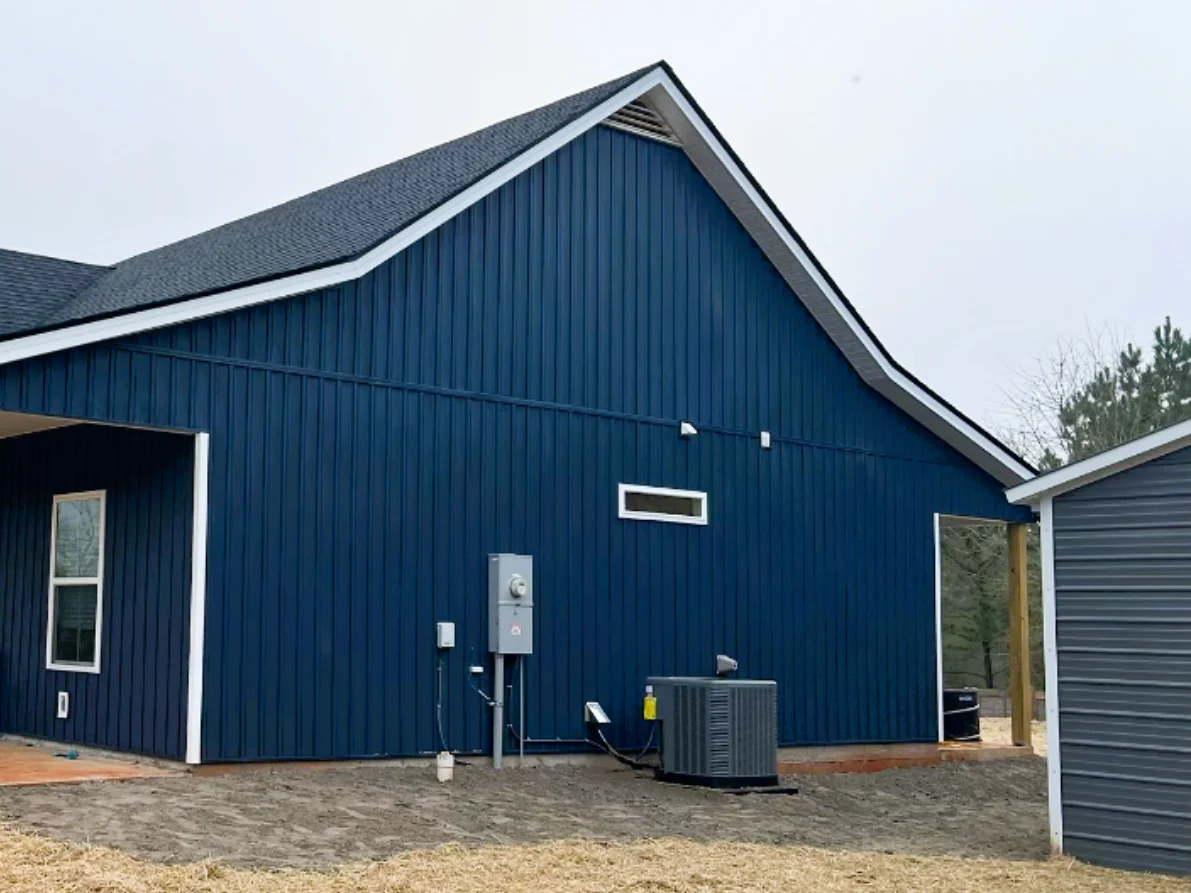 A large residential exterior wall features deep blue vertical board-and-batten panels contrasted by crisp white trim, highlighting a modern and dramatic siding replacement project.