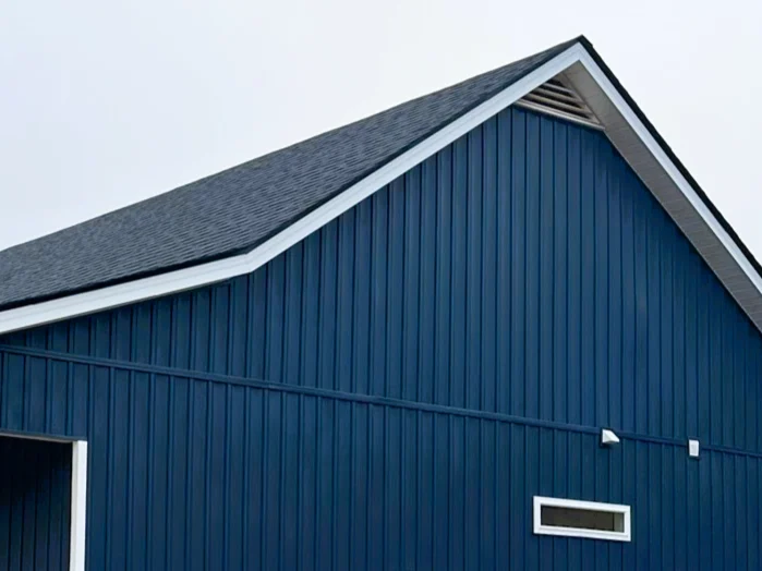 A large residential gabled roof with clean, dark shingles stands out in sharp contrast against vivid blue vertical siding, highlighting professional roofing services.