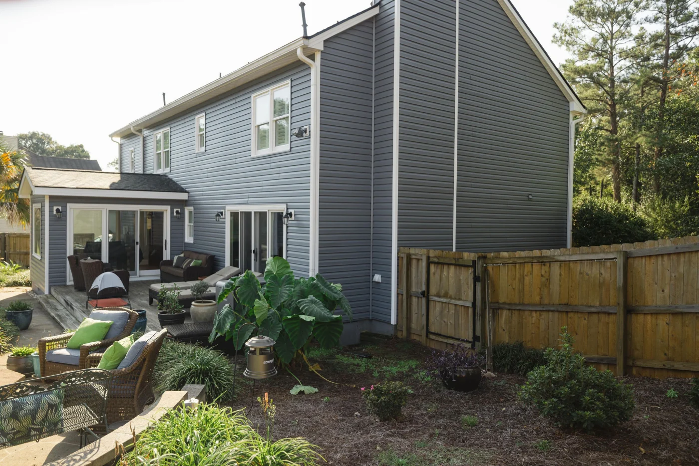 The backyard view of a multi-story home reveals a comprehensive siding replacement featuring clean gray horizontal planks and crisp white corner trim that perfectly frames the outdoor patio and living space.