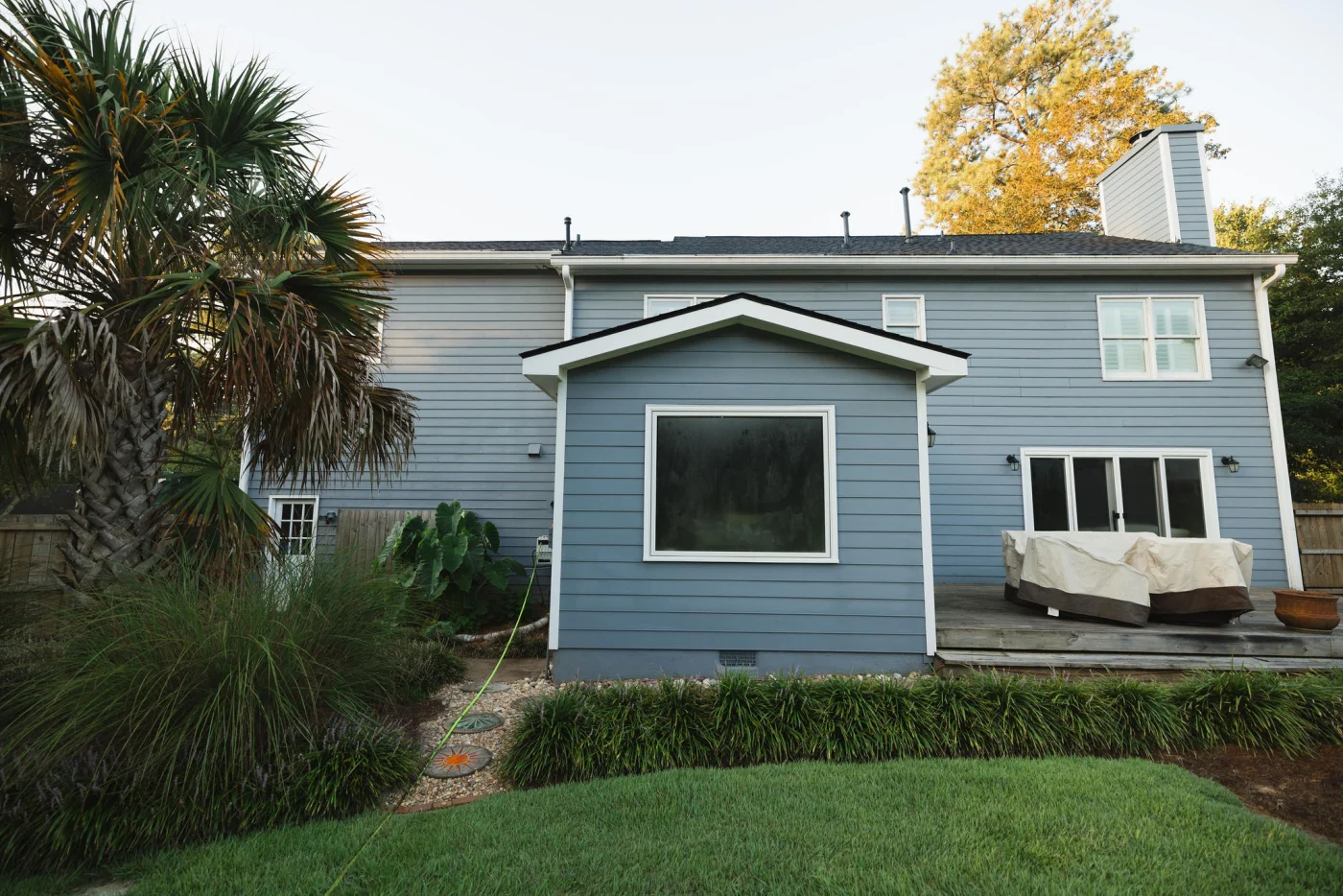 The back profile of this two-story home shows a large, modern replacement window installed on a bump-out section wrapped in blue siding next to a backyard deck.