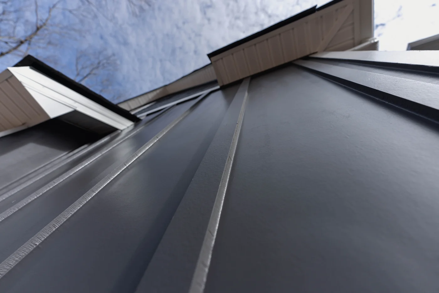 A dramatic low-angle view looking up a home exterior showcases the flawless installation of dark gray vertical board-and-batten siding underneath a crisp white roofline soffit, demonstrating a professional siding service.