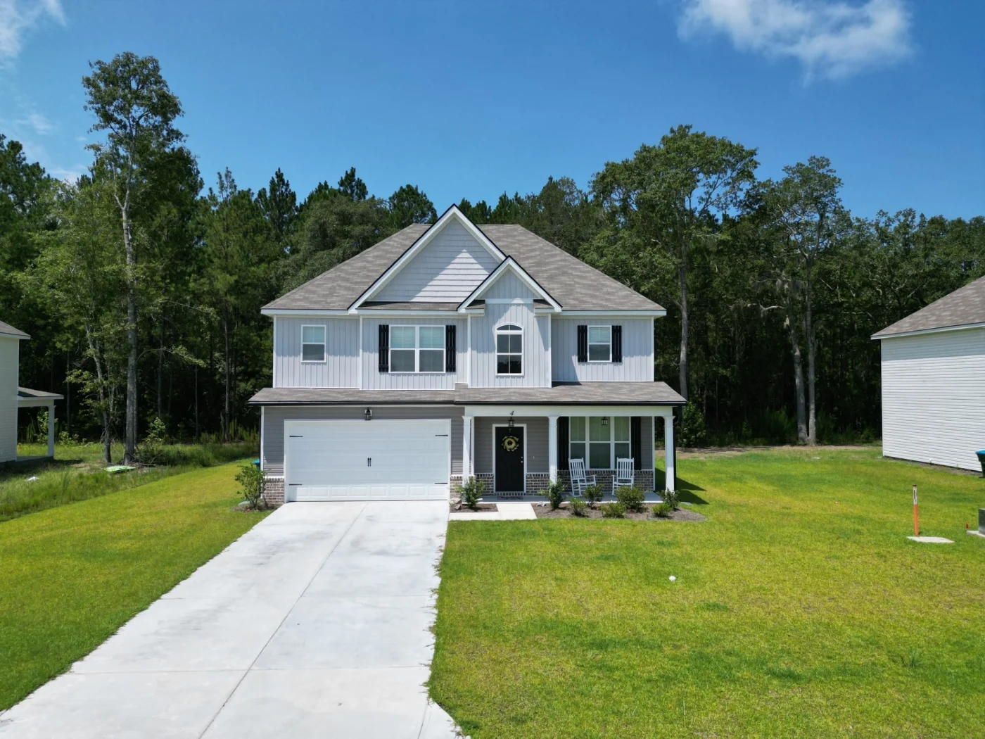 A wide aerial view showcases a newly built two-story home with light gray siding, black shutters, a spacious two-car garage, and a fresh concrete driveway, highlighting expert new construction services.